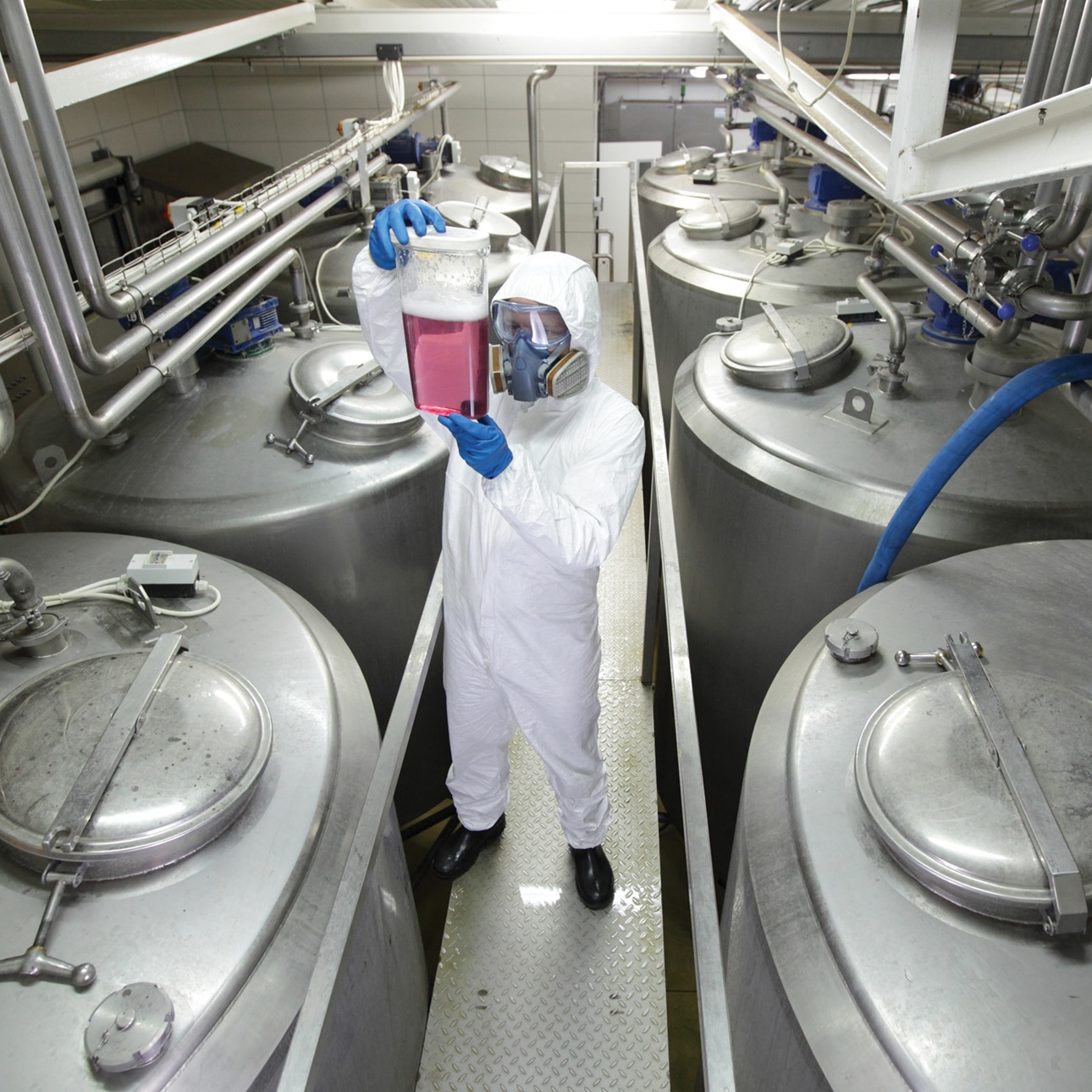Specialist in protective uniform, mask, goggles, gloves and wellies controlling industrial process,examining sample.