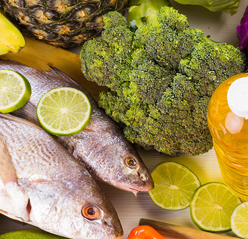 Variety of food including fresh fish, limes, broccoli, pineapple, peppers, and oil.