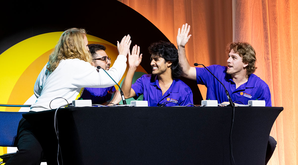 The winning Clemson University food science team of four sitting at a table high fiving each other at IFT FIRST.
