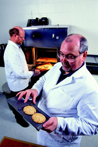 Cookie-baking test reveals whether wheat has the desired characteristics to make tender pastry products. Here, food technologist Ron Martin (left) removes test cookies from the oven while food technologist Charles Gaines measures two cookies.