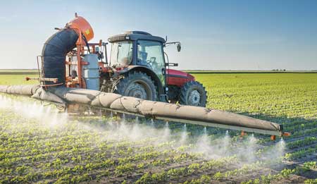 Tractor sprays a crop with pesticide.
