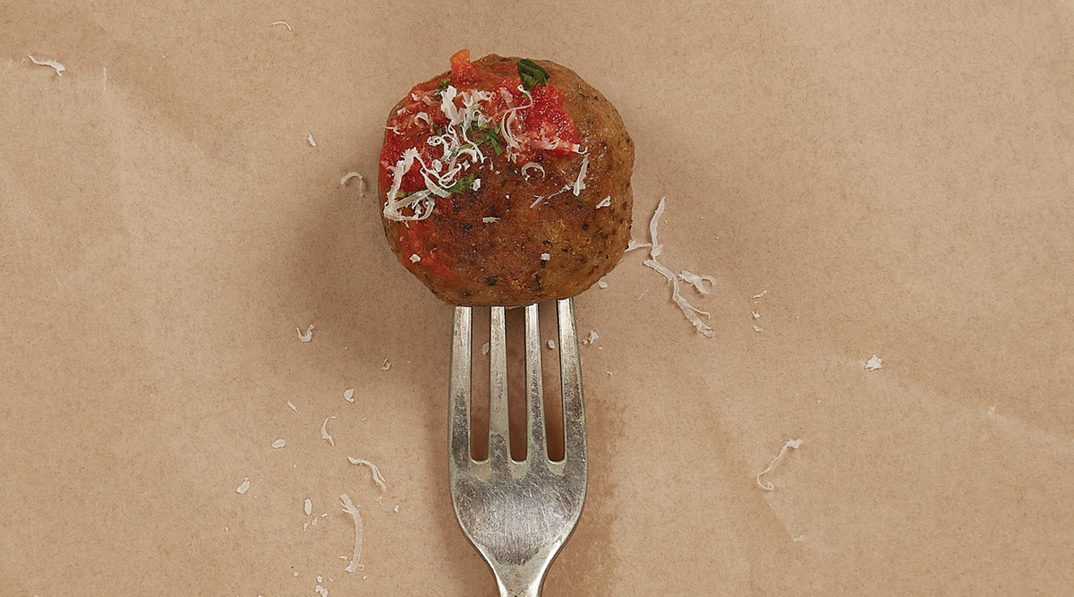 Fork through an Ivy Farm meatball with grated cheese, greens, and tomato on top