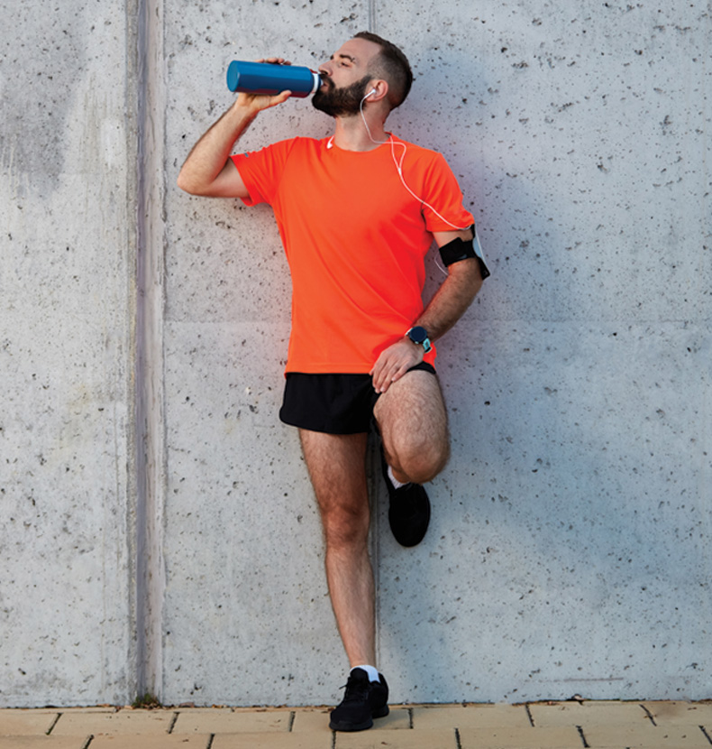 Man resting from running and drinking water while standing against the wall