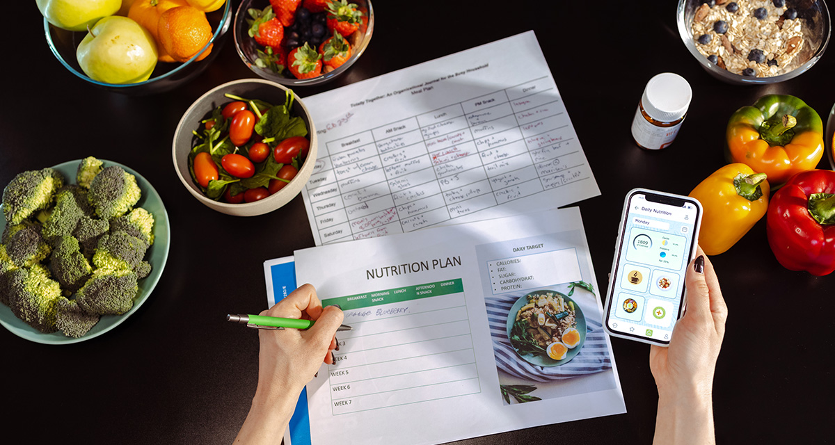 a woman's hands are shown filling out a nutrition log and using a smart phone