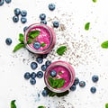 Pink blueberry smoothies surrounded by scattered blueberries and leaves