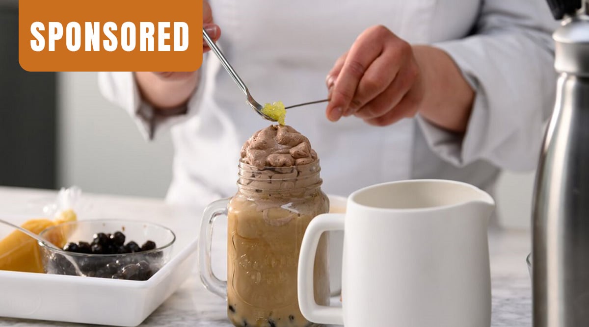 Person adding yellow pearls on top of Boba drink