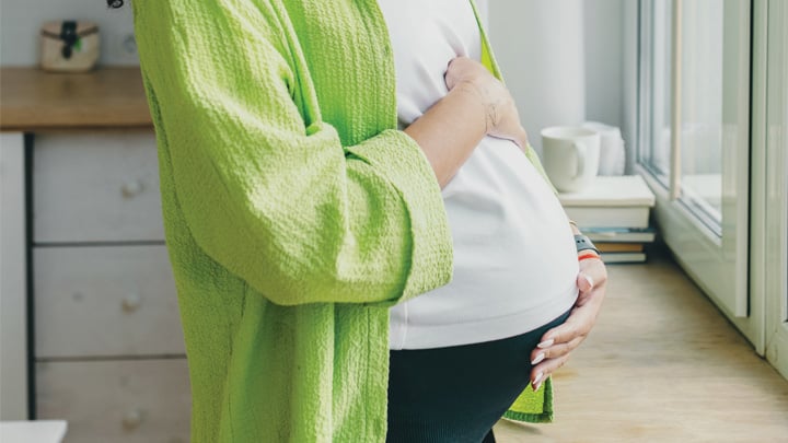 Pregnant woman stroking her tummy standing in front of big window