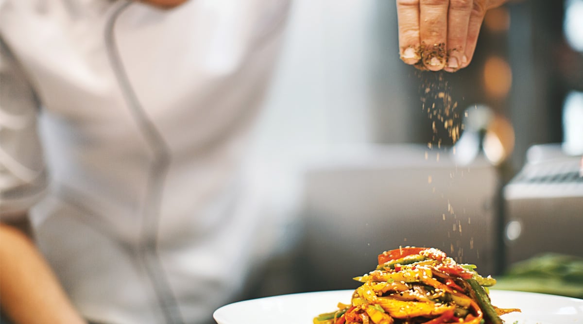 Chef sprinkling spices on a dish.