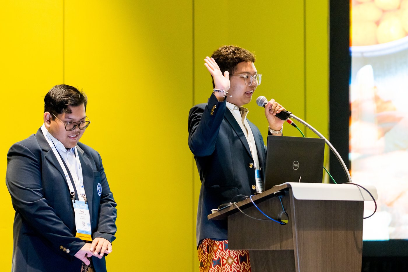 Two students on stage with one speaking at a podium at IFT FIRST.