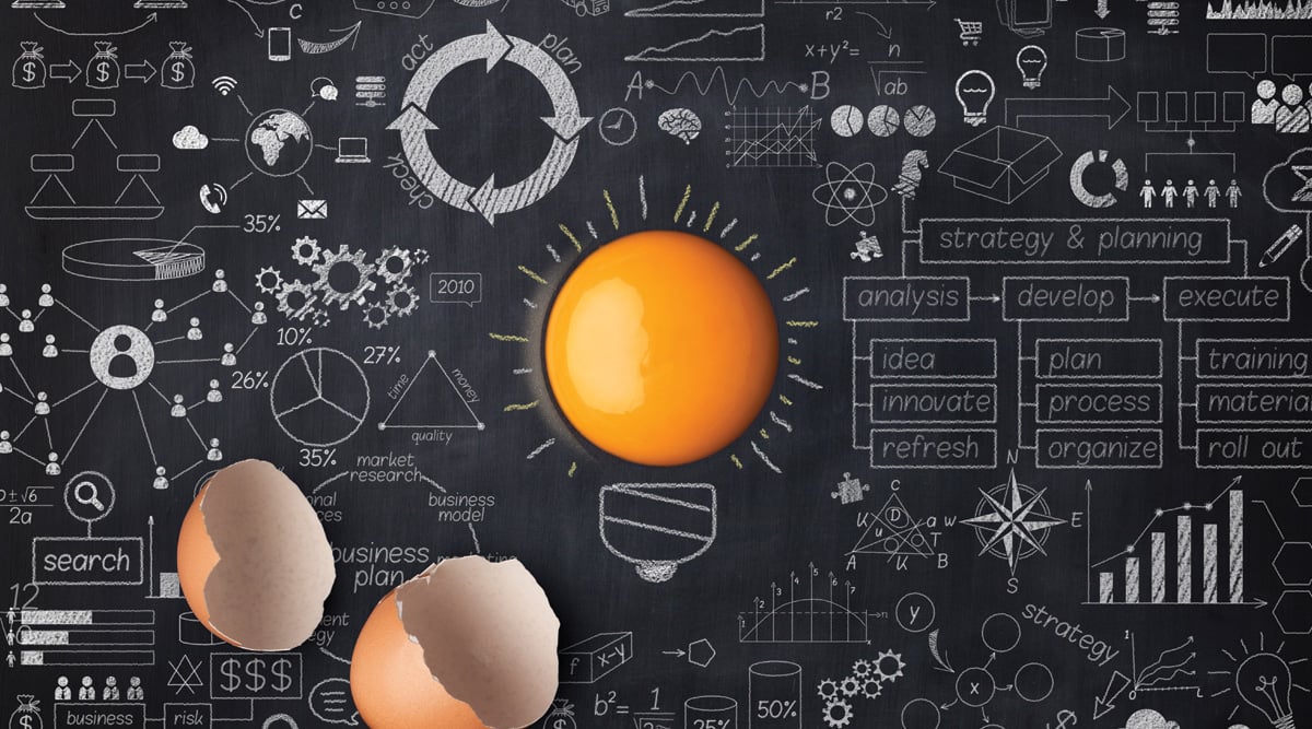 Egg yolk ball forming a shape of illuminated light bulb on blackboard