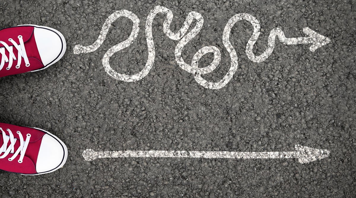 Red sneakers pointing to two different chalk arrows on a road.
