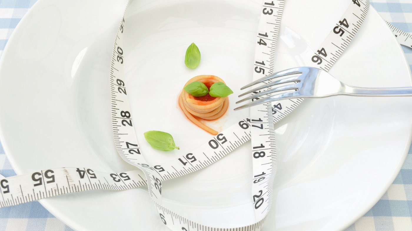 A plate with a tiny amount of food and a tape measure and fork on top.