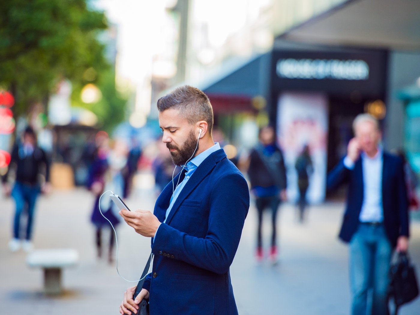 Man on street looking at phone with headphones in
