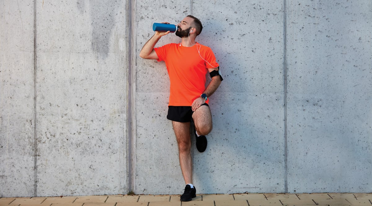 Man resting from running and drinking water while standing against the wall