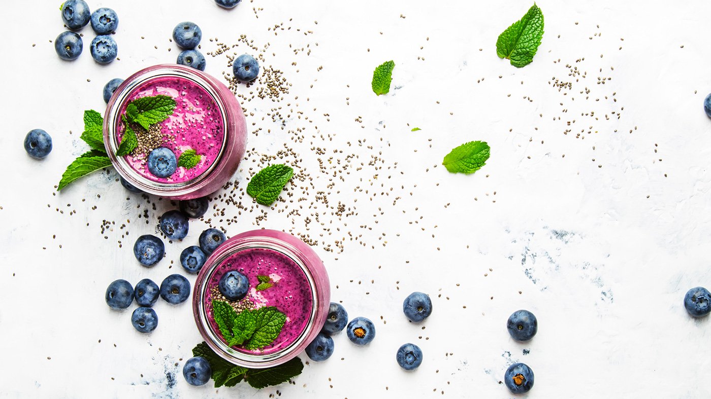 Pink blueberry smoothies surrounded by scattered blueberries and leaves