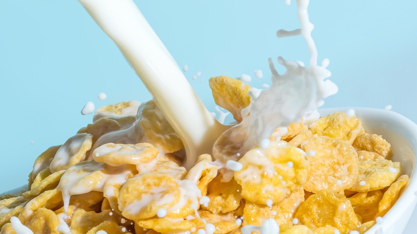 Milk stream pouring into a bowl with сornflakes.