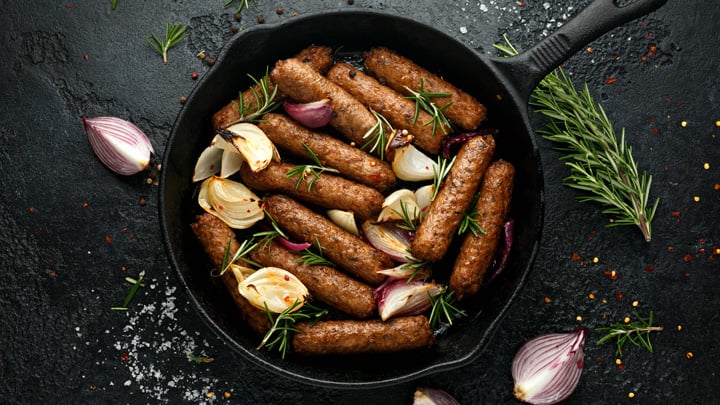 Rosemary and onion vegetarian vegan sausages oven baked in cast iron skillet frying pan.