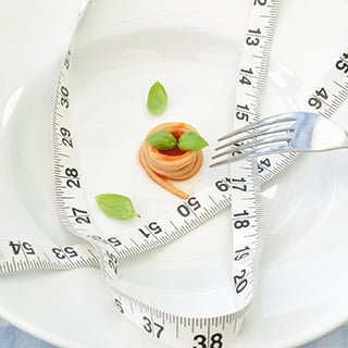 A plate with a tiny amount of food and a tape measure and fork on top.