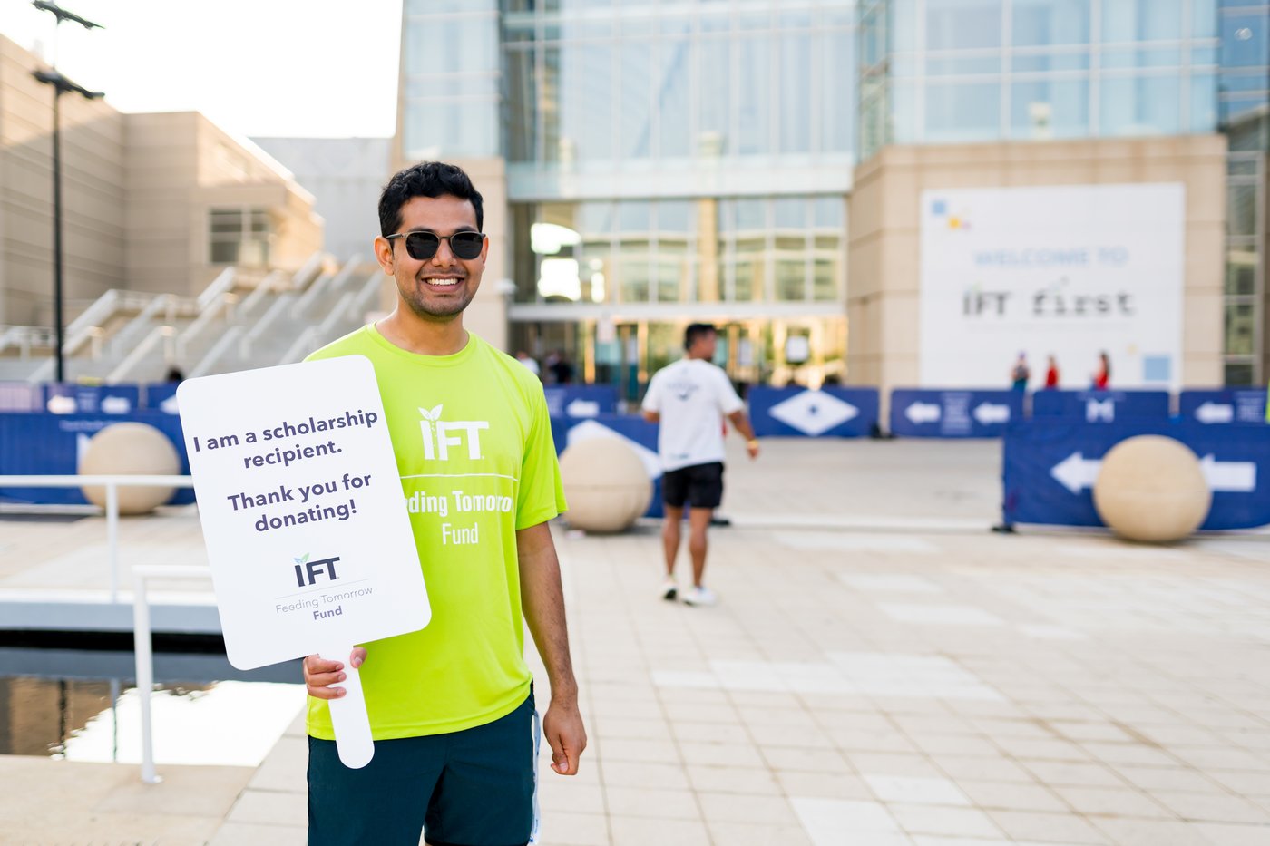 Smiling student standing outside McCormick Place holding a sign stating that they are an IFT Feeding Tomorrow Fund Scholarship recipient.