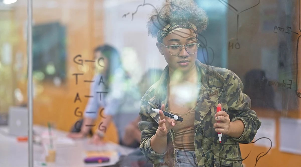College student writing on a transparent whiteboard in a classroom.