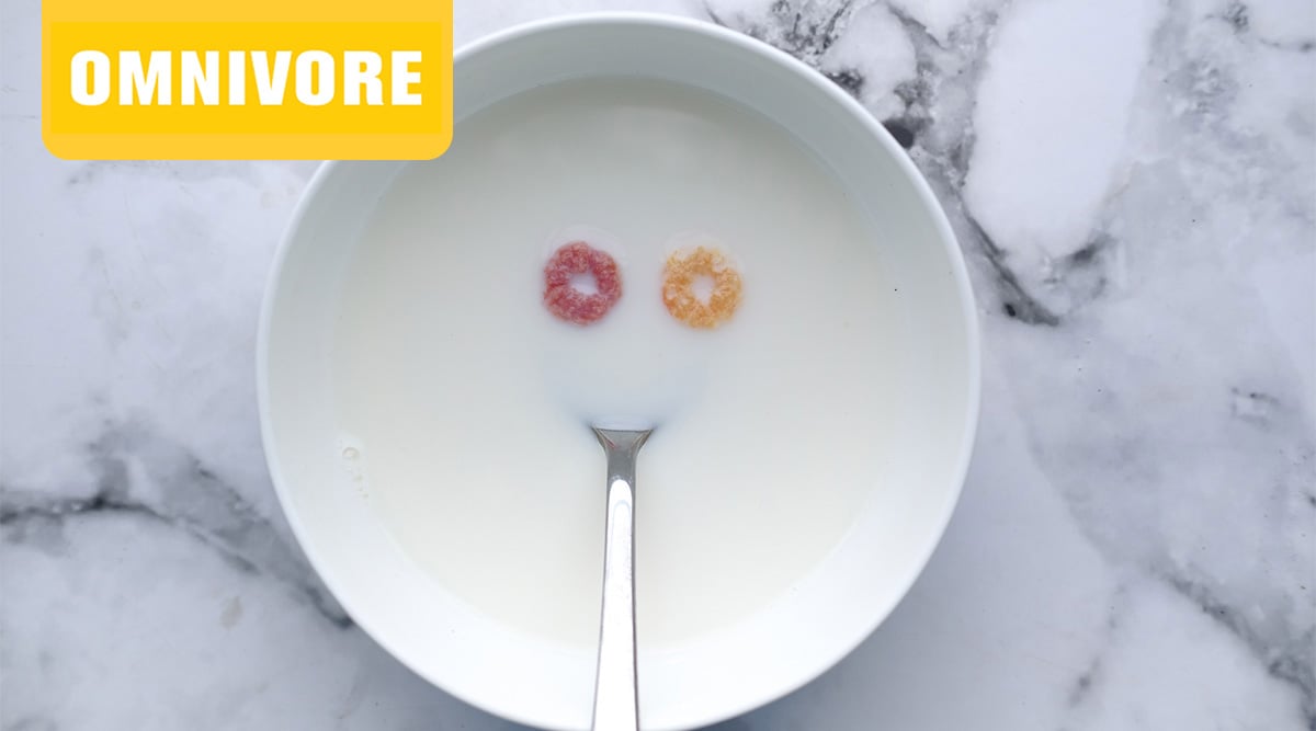 A bowl of milk with two pieces of cereal and a silver spoon.