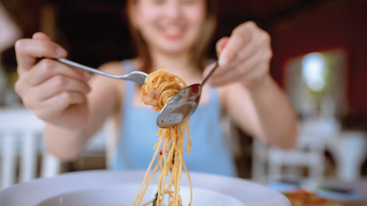 Young Asian woman rolling spaghetti while eating lunch in Italian cafe.