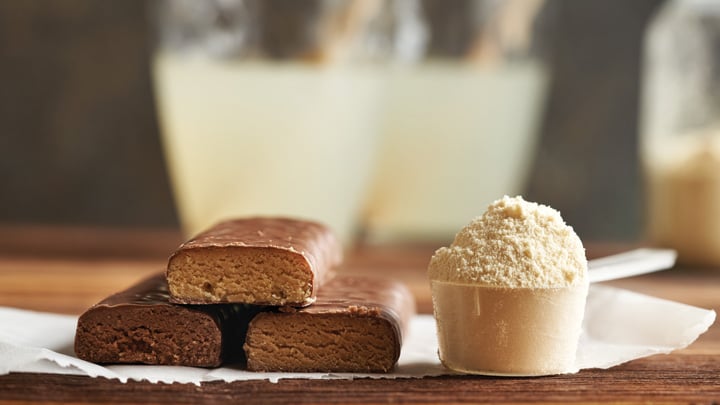 Three healthy vegetarian protein chocolate bars with whey protein powder and drink.