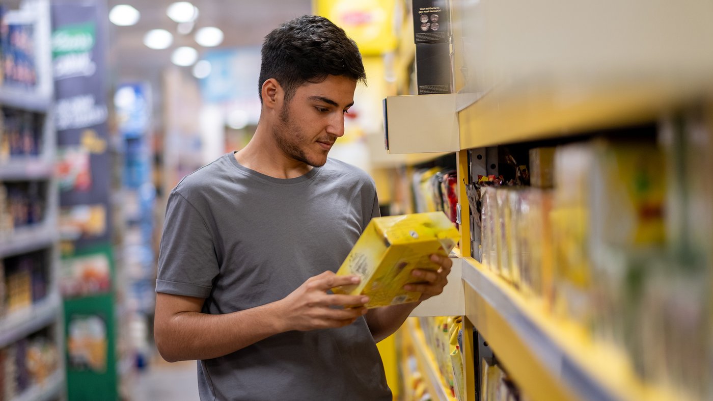 Young man choosing products in supermarket reading label carefully