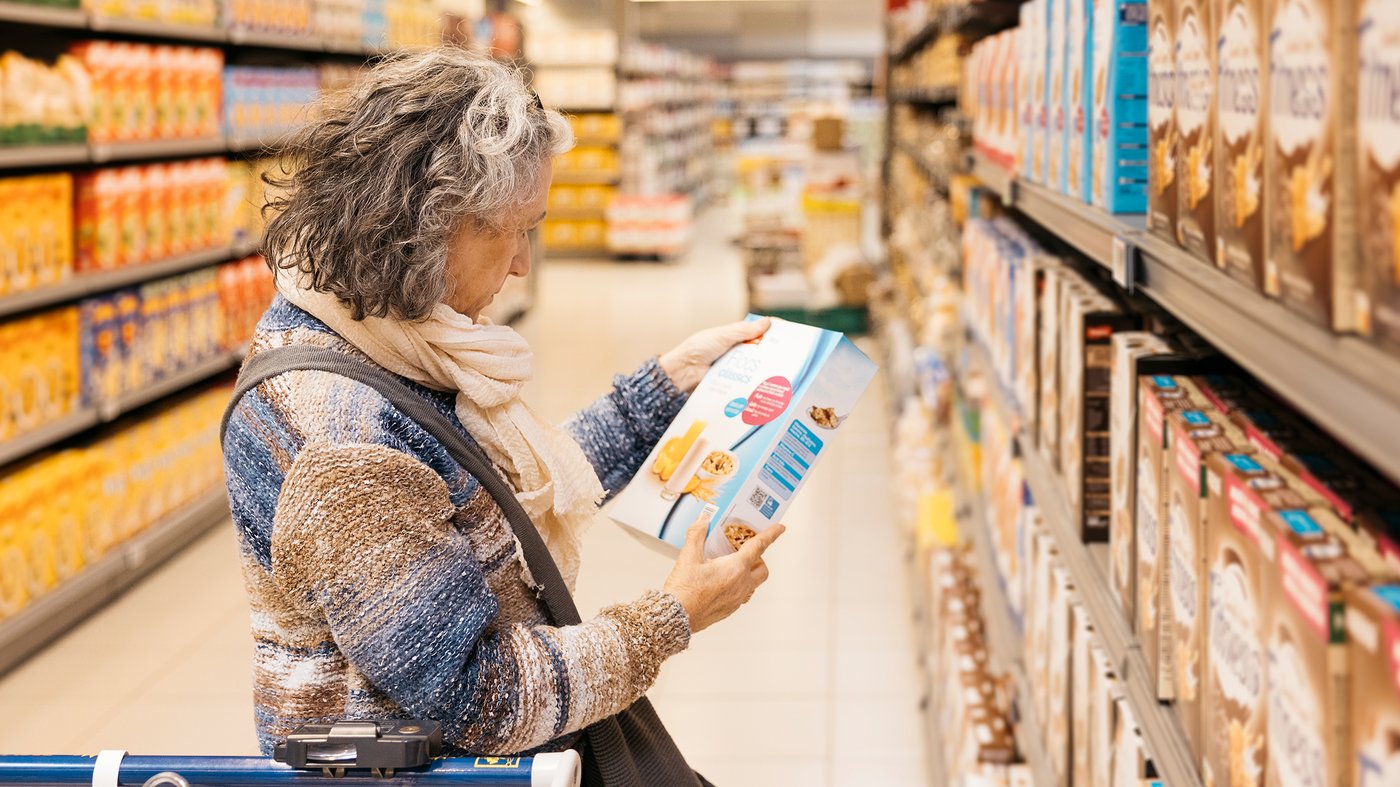 Senior adult woman examining cereal box label at supermarket