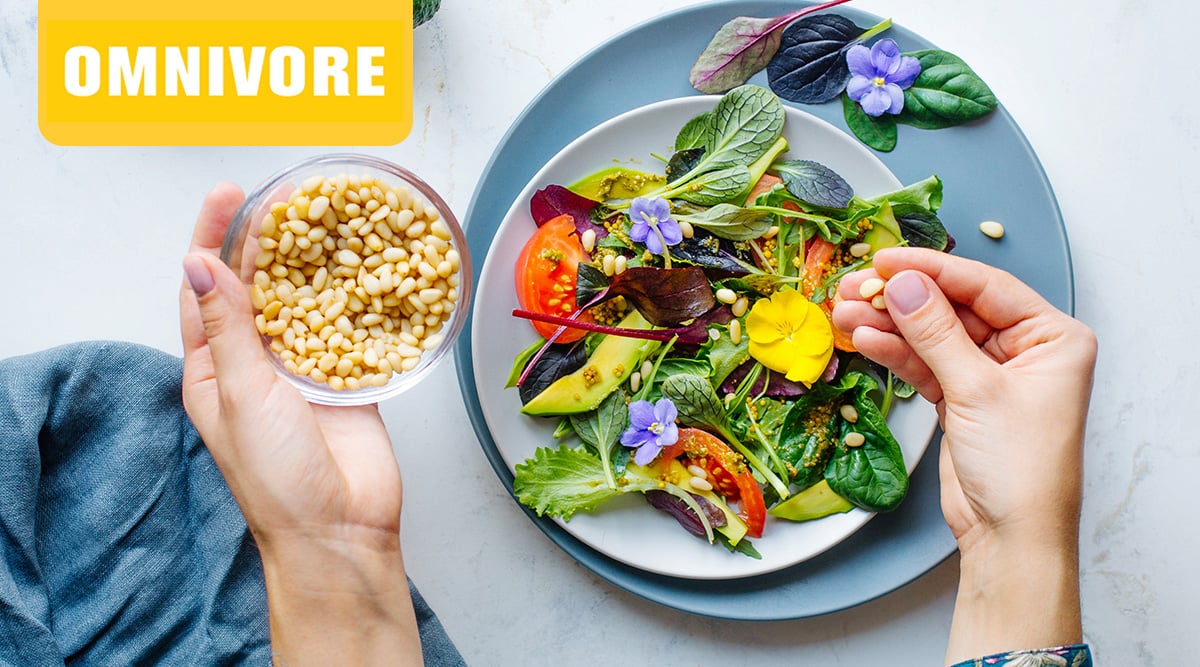 Hands adding pine nuts to a colorful salad.