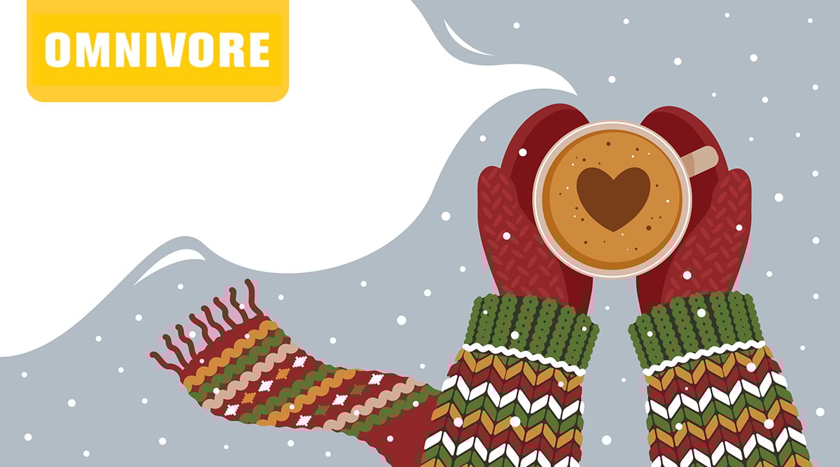 Person wearing a holiday sweater, scarf, and mittens holding hot cocoa with a heart out in the snow.