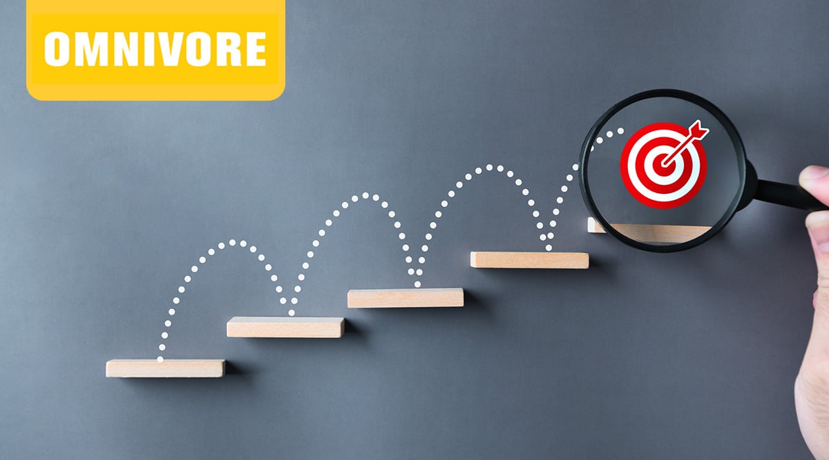 A bullseye target at the top of steps with a magnifying glass over it.