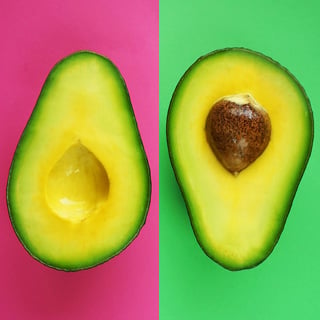 Halves of cut ripe avocado on pink and green background.