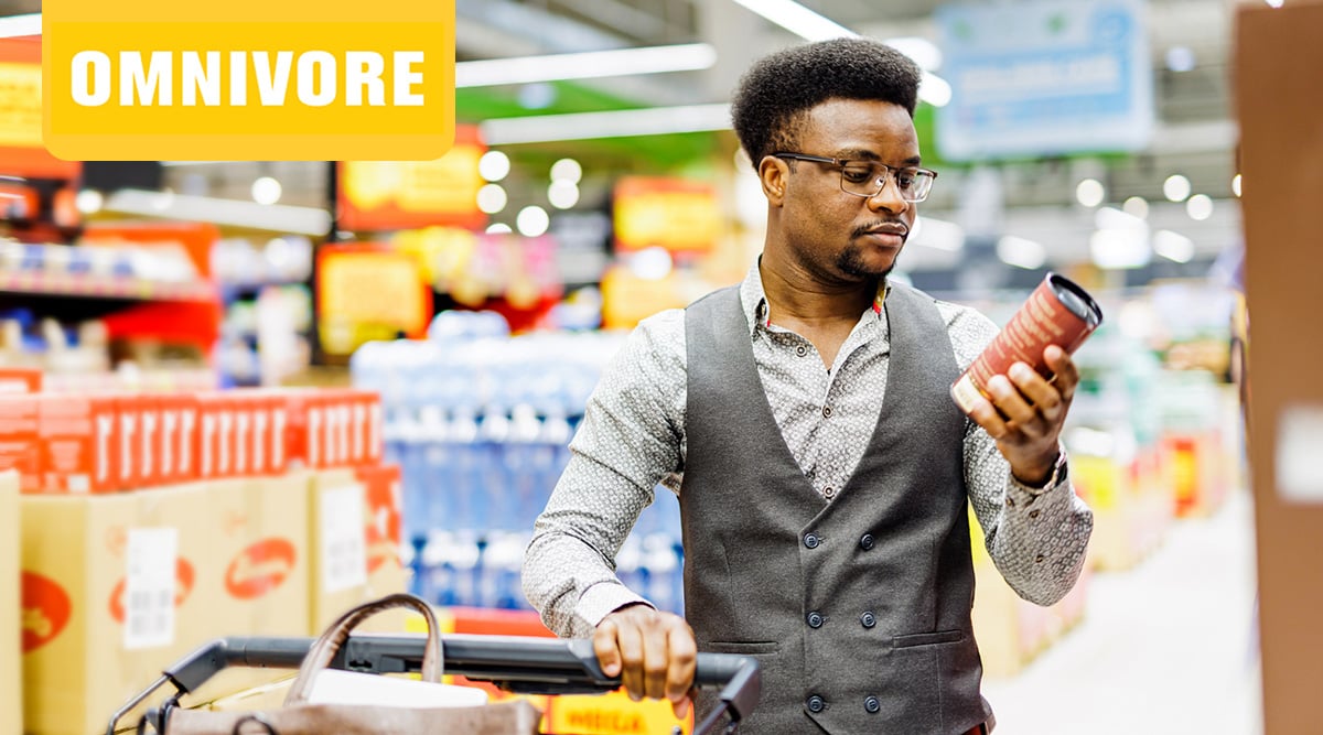 A man with a cart looking at a product at the grocery store.