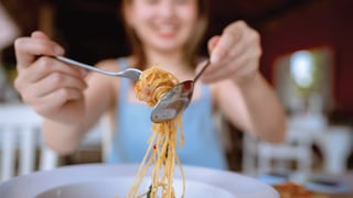 Young Asian woman rolling spaghetti while eating lunch in Italian cafe.