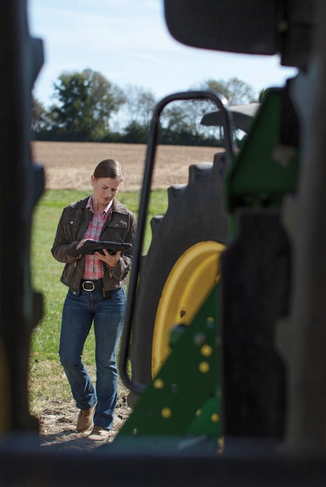 Farmer with a Digital Device Behind a Tractor