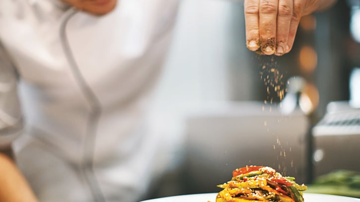 Chef sprinkling spices on a dish.