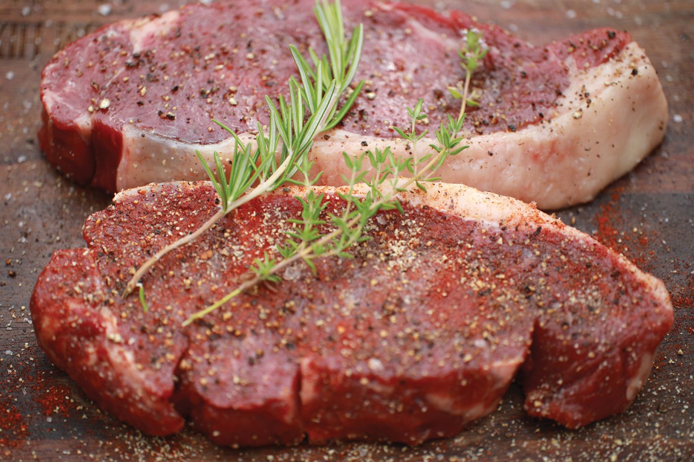 A plate of succulent marinated steaks seasoned with pepper, salt, and herbs, ready to be cooked