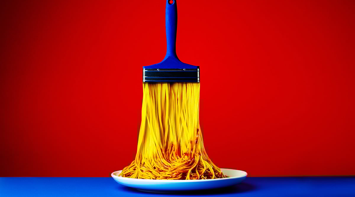 Paint brush with pasta as the bristles going onto a plate.