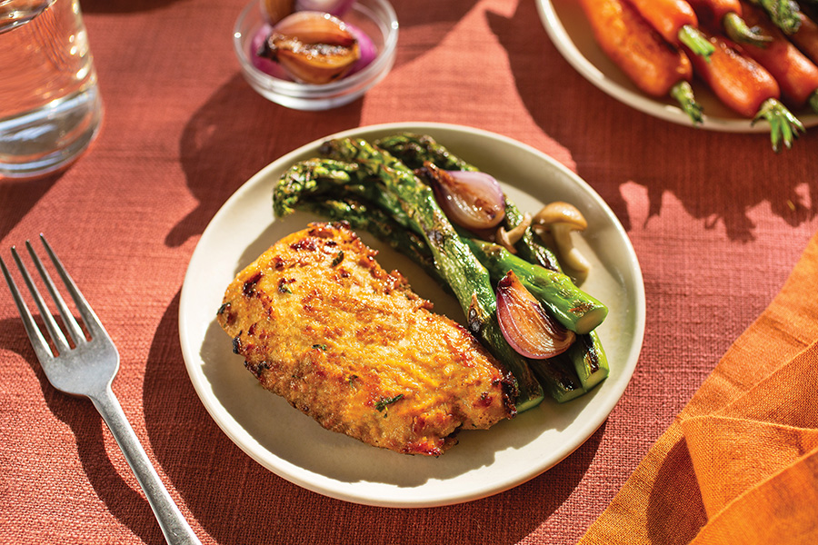 Plate of UPSIDE Foods chicken, asparagus, shallots, and mushrooms with a fork on the side on top of a table setting